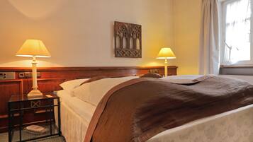 A hotel room with a bed, two bedside tables with lamps, a decorative wall piece, and a window with curtains.