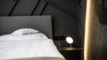 A neatly made bed with white linens and a headboard, a bedside table with a round lamp, and a dark wall with geometric patterns.