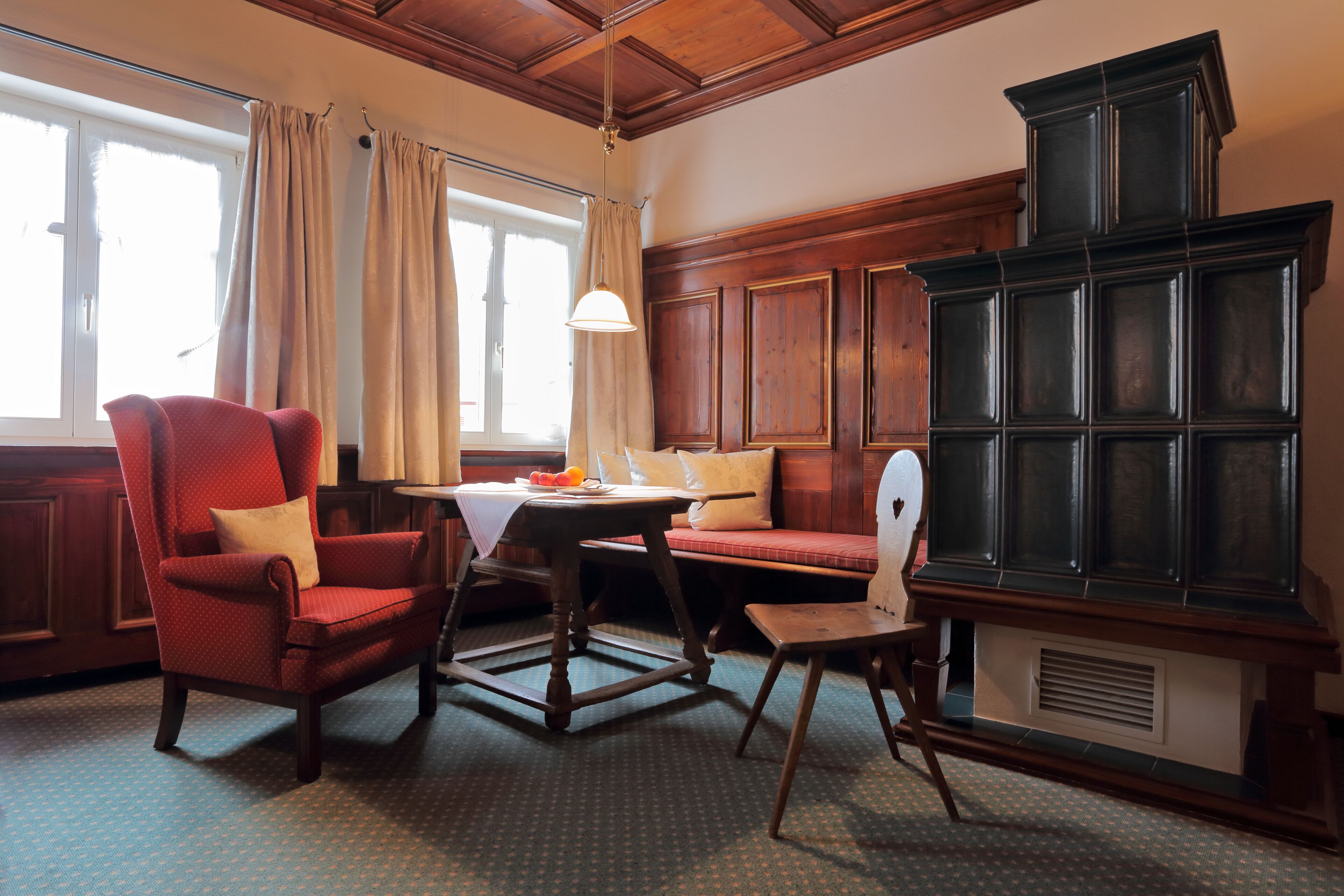 A room with a wooden bench, a red armchair, a small table with a white tablecloth, and a large dark wooden cabinet.