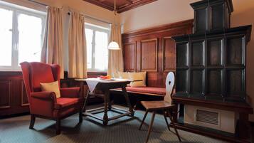 Una habitación con un banco de madera, un sillón rojo, una mesita con mantel blanco y un mueble de madera oscuro y grande.