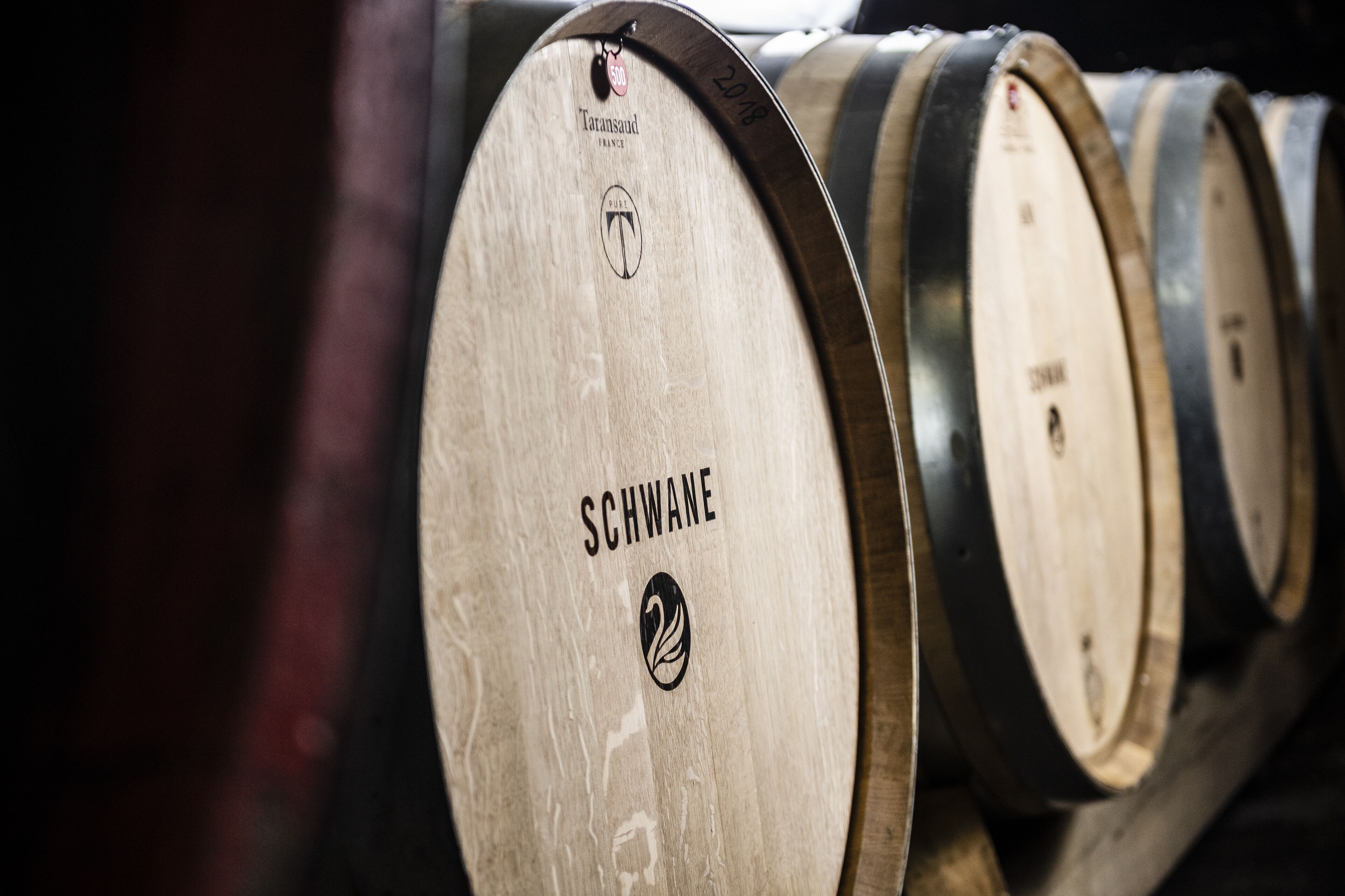 Wooden barrels with the label "Schwane" and a logo, arranged in a row.