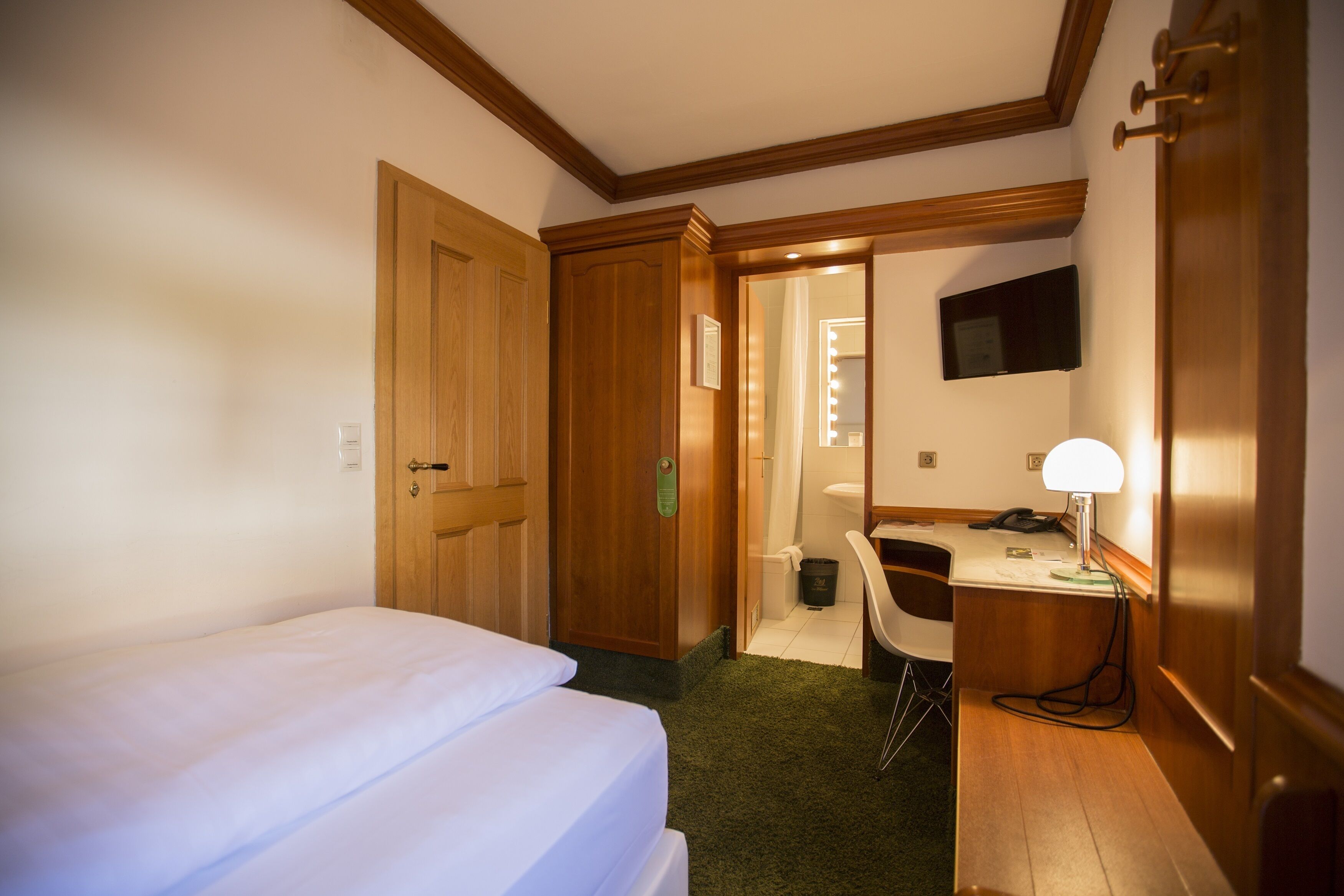 Ein Hotelzimmer mit Bett, Schreibtisch, Sessel, Fernseher und Spiegel.