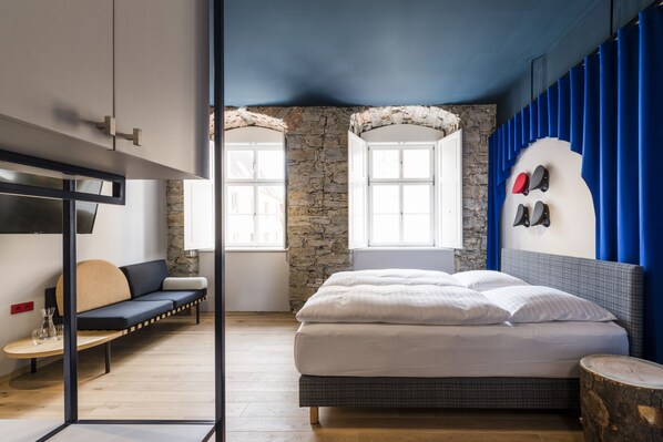 Un dormitorio moderno con pared de piedra, cama con ropa de cama blanca, pared de acento azul y vistas por una ventana.