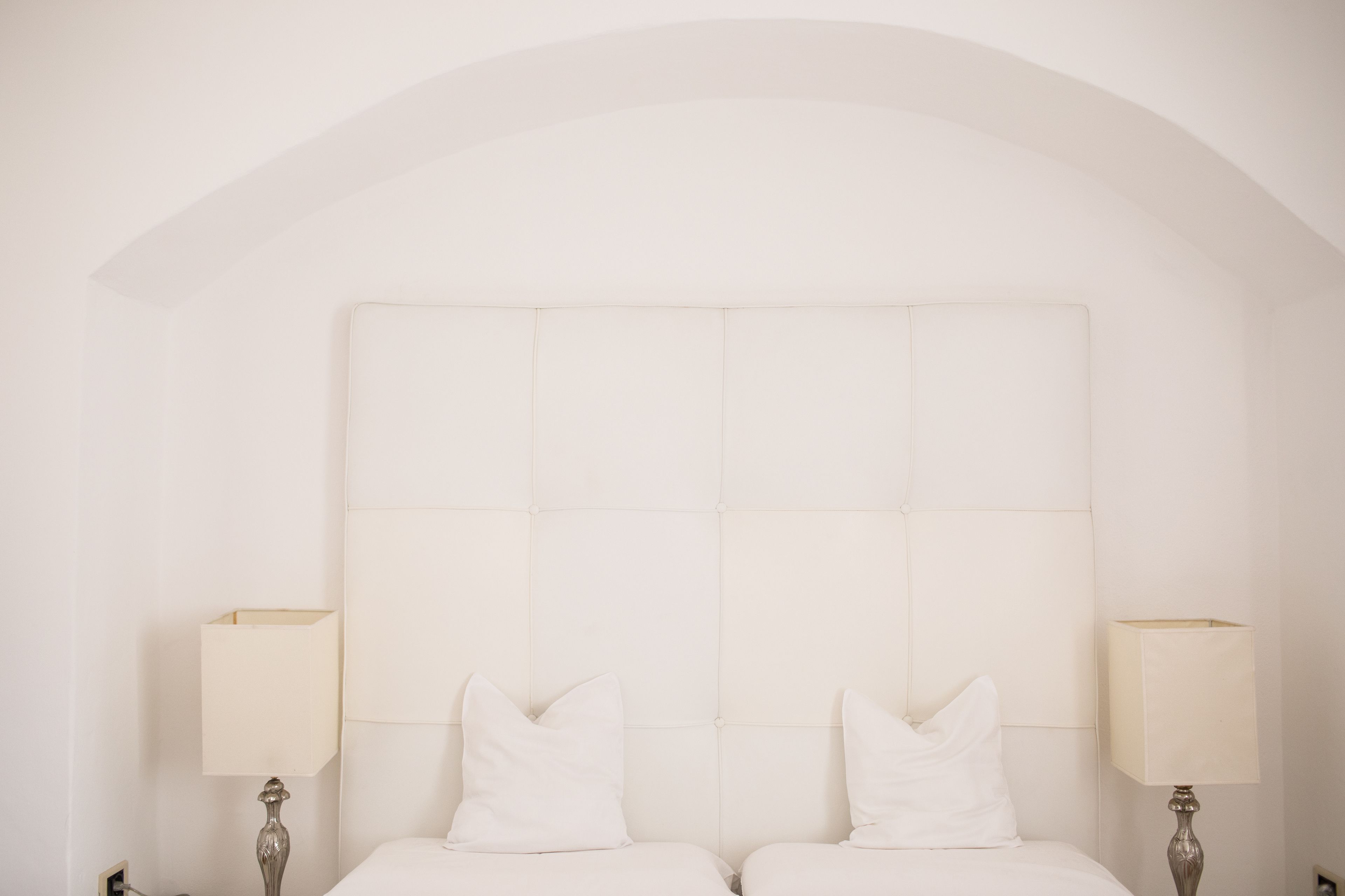 A bedroom with a large, square headboard, two bedside tables with lamps, and two pillows on the bed.
