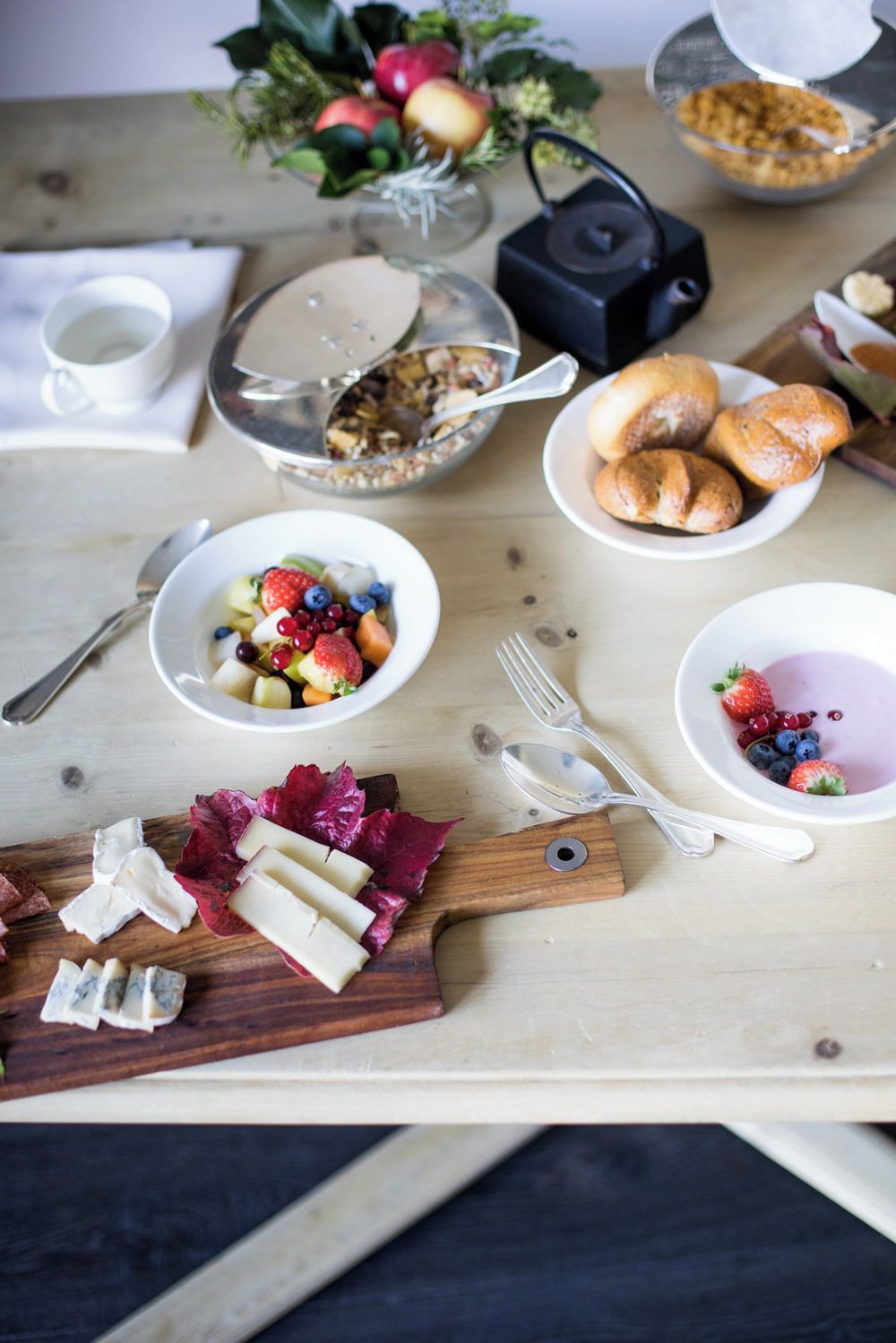 A breakfast table with various food items including fruits, pastries, and cheese.