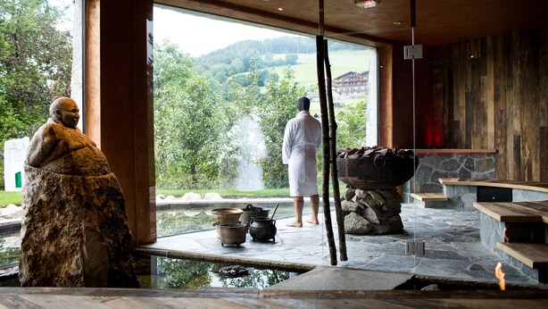 A stone-floored outdoor area with a hot tub, a stone fireplace, and a view of a mountainous landscape. - Romantik Hotel Turm (Fie allo Sciliar)