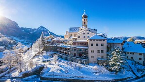 A historic town with a prominent church featuring a tall tower, surrounded by snow-covered buildings and mountains in the background. - Romantik Hotel Turm (Fie allo Sciliar)