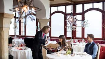 Un restaurante con mesas preparadas para comer, un camarero atendiendo una carta y vistas del cielo a través de amplios ventanales.