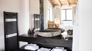 A modern bathroom with a large stone sink, black towel racks, and a wooden ceiling. - Romantik Hotel Turm (Fie allo Sciliar)