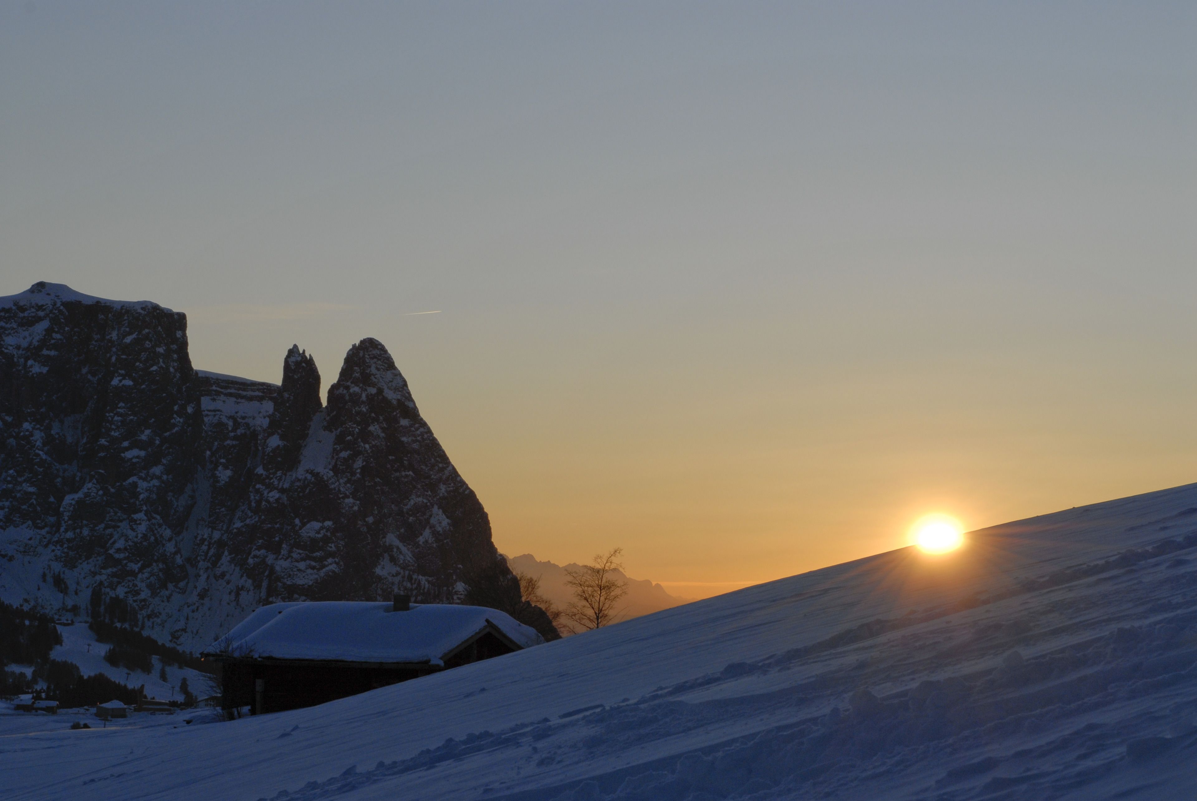 Eine verschneite Berglandschaft im Abendrot mit einer Hütte.