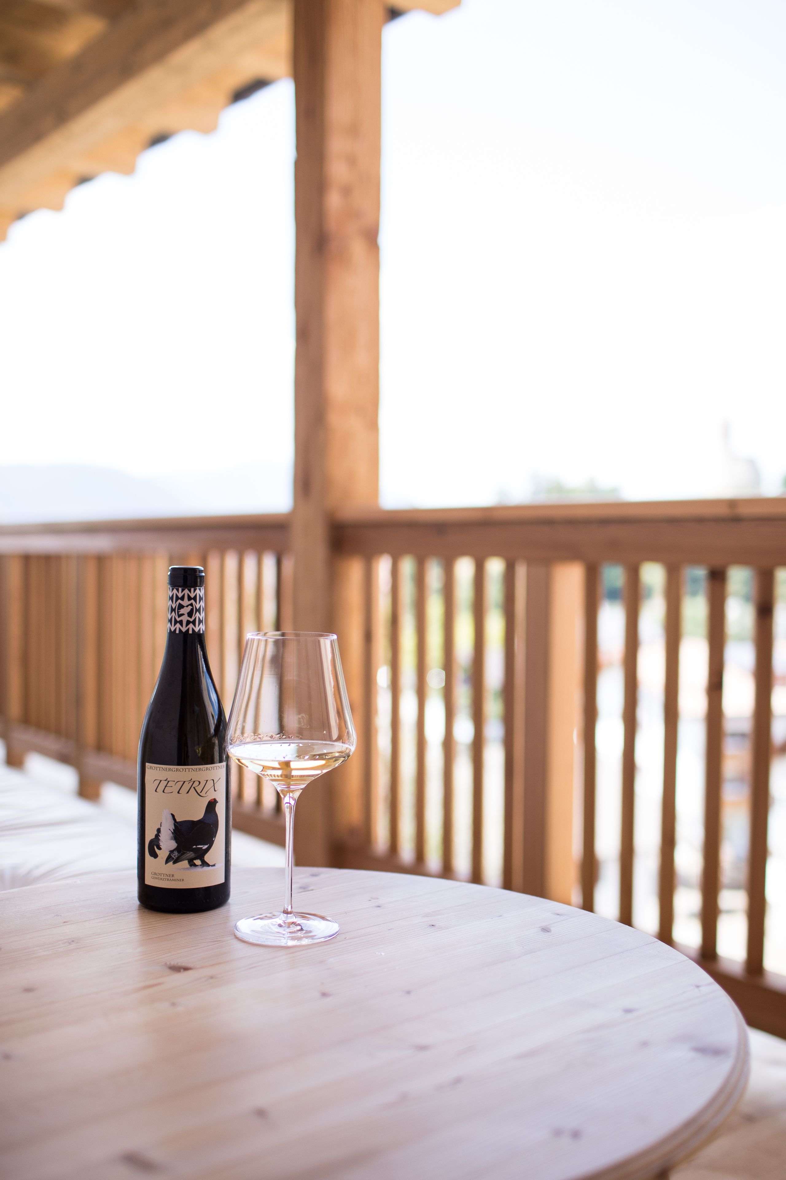 A bottle of wine and a glass on a wooden table outdoors.