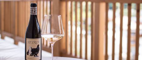 A bottle of wine and a glass on a wooden table outdoors.