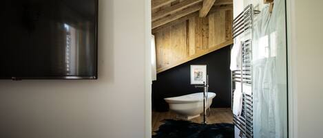 Un baño moderno con techo de madera, una bañera independiente, cabina de ducha de vidrio y un televisor montado.