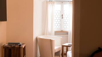 Ein Schlafzimmer mit Holzboden, einem weißen Bett, einem kleinen Tisch und einem Fenster mit Vorhängen.