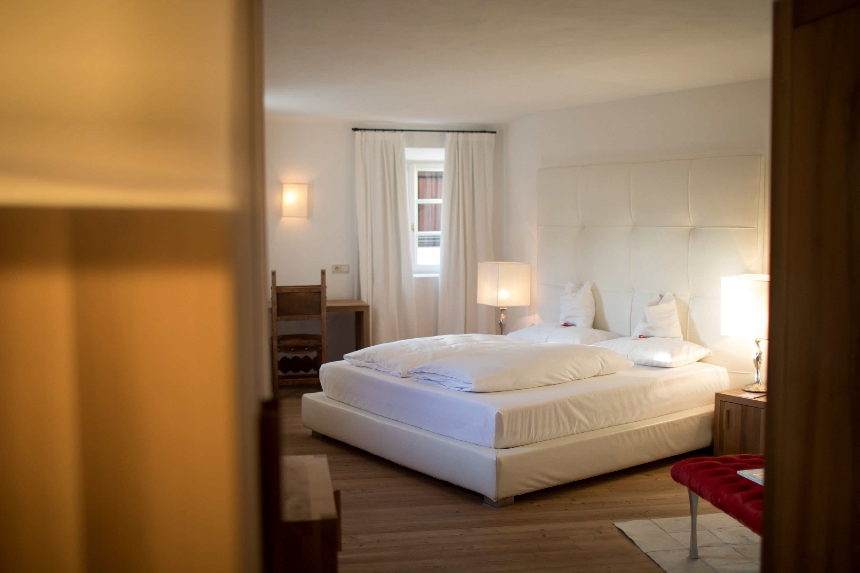 Una habitación de hotel moderna con una cama grande, lámparas de noche, suelo de madera y vistas a la ciudad por la ventana.
