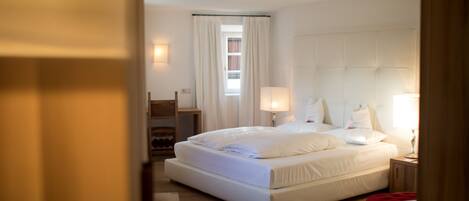 Una habitación de hotel moderna con una cama grande, lámparas de noche, suelo de madera y vistas a la ciudad por la ventana.