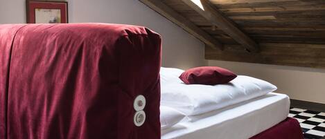 Una habitación con tragaluz, cama con cubre color rojo y piso a cuadros.
