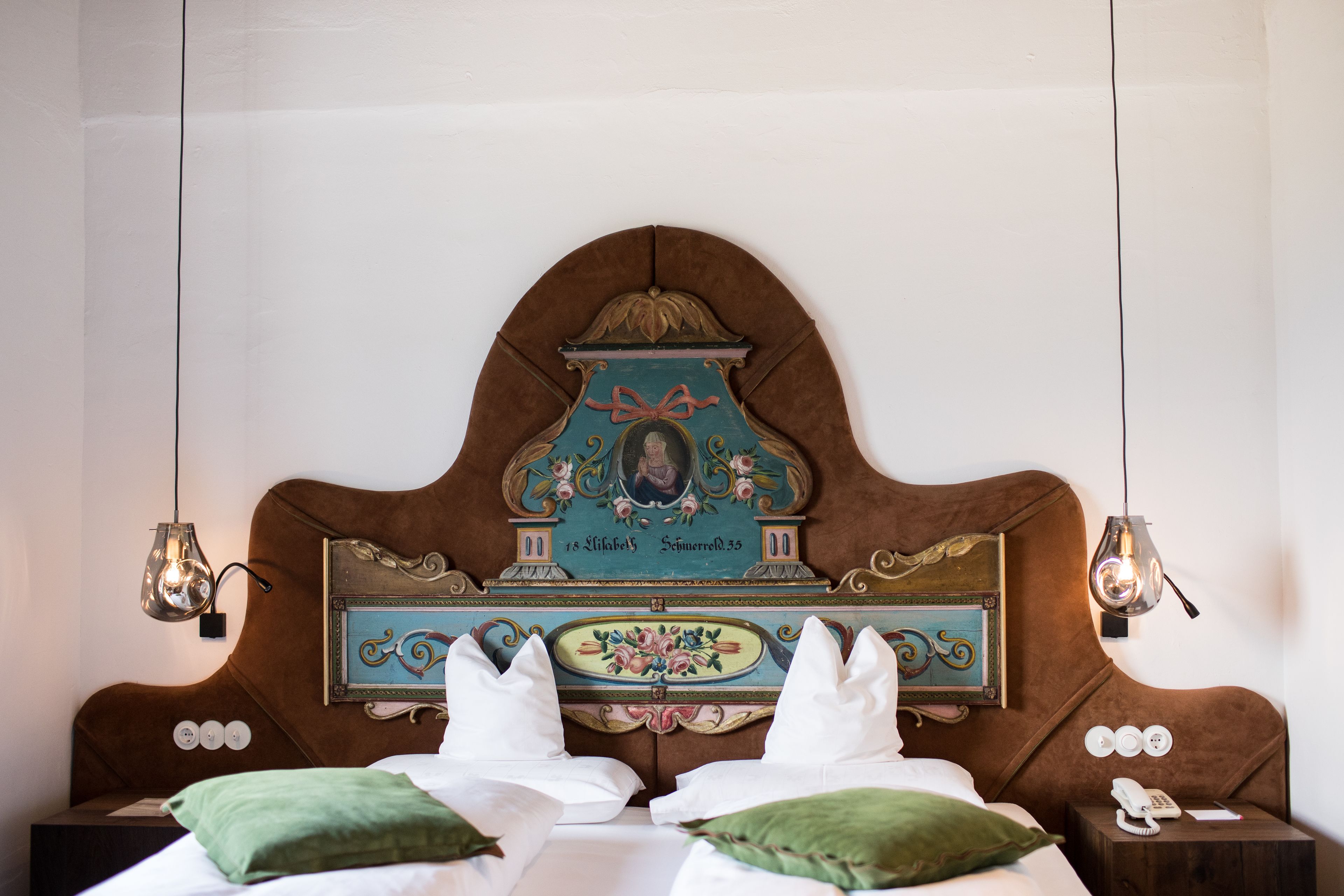A bed with a headboard featuring a decorative plaque, two bedside lamps, and a nightstand with a phone.