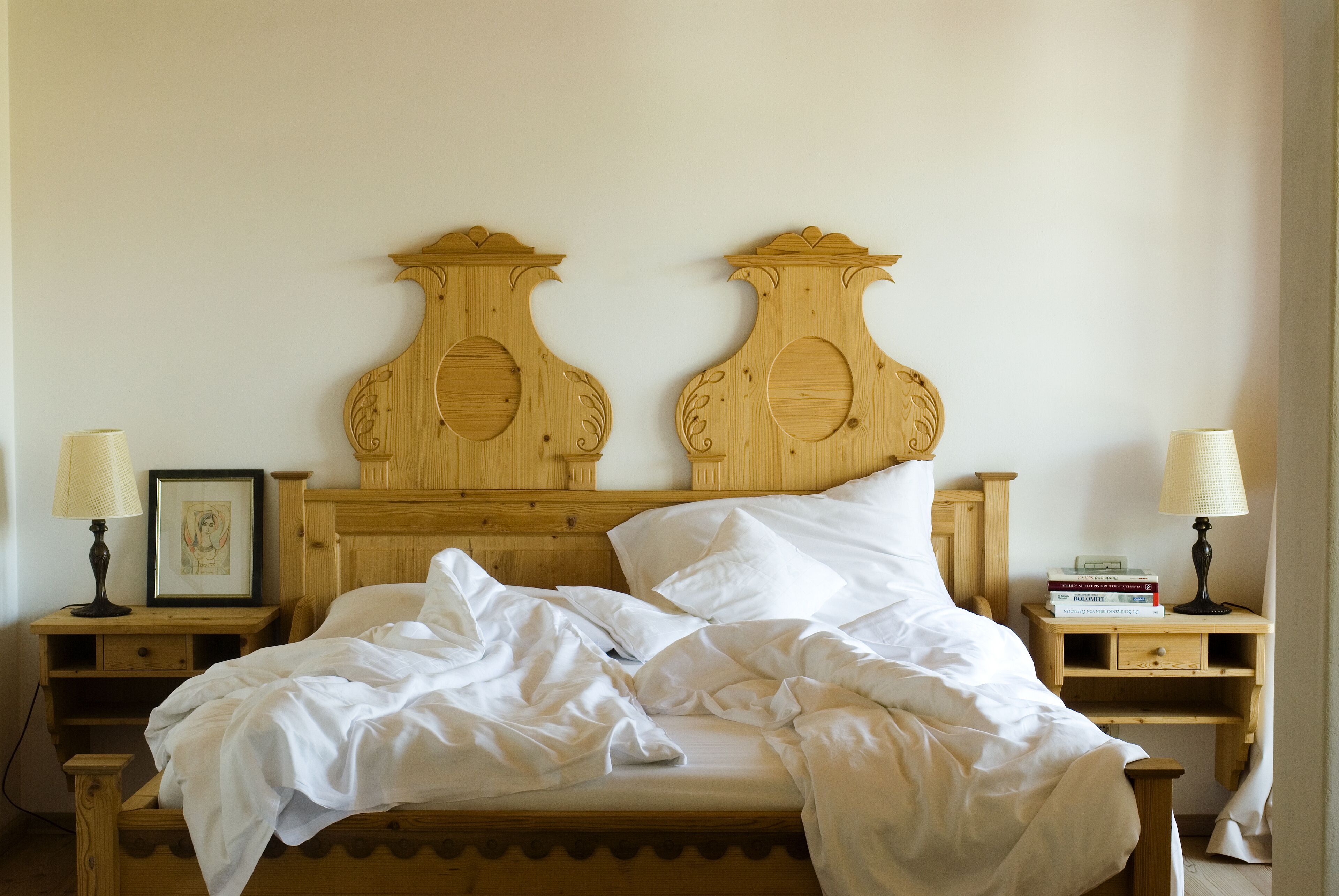 A wooden bed with a carved headboard, two bedside tables with lamps, and a framed picture on one table.
