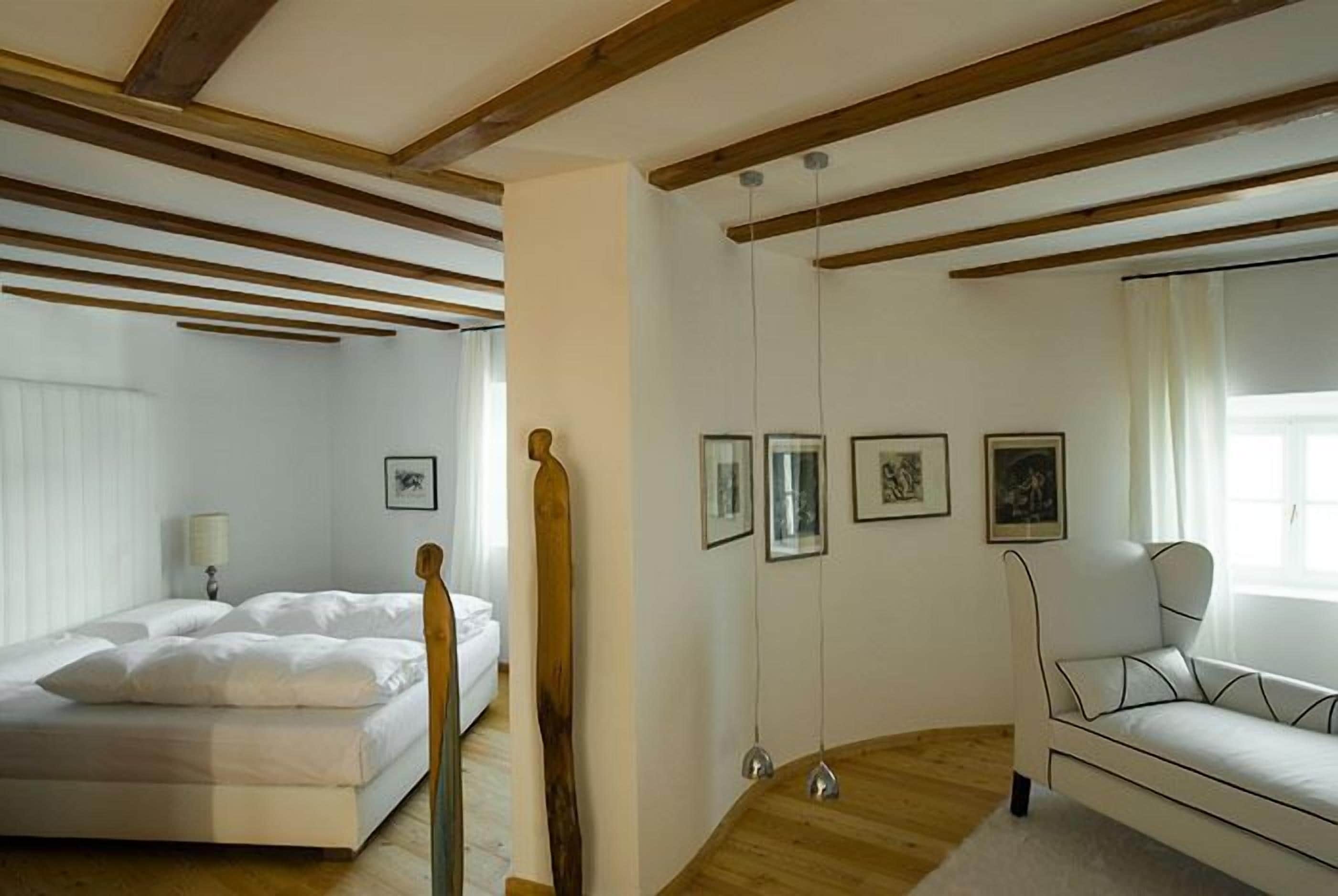 Una habitación con cama, sofá, vigas de madera en el techo y cuadros enmarcados en la pared.