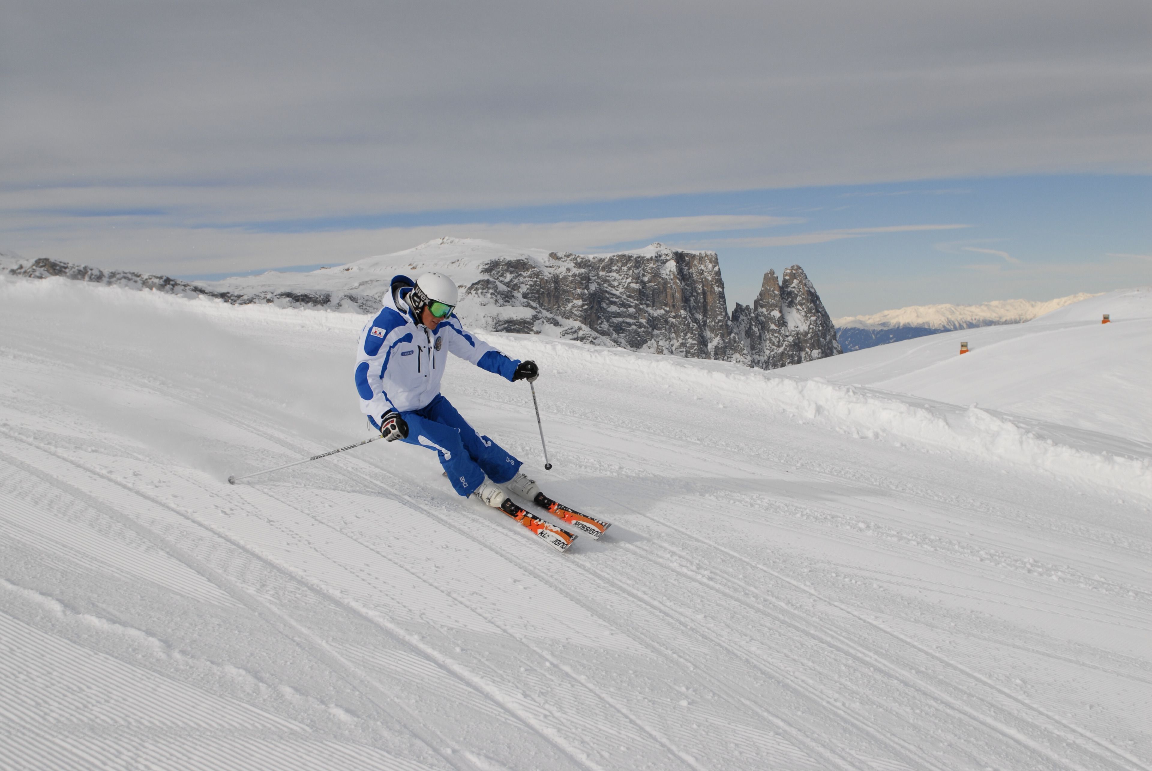 Uno sciatore su una pista innevata con montagne rocciose sullo sfondo.