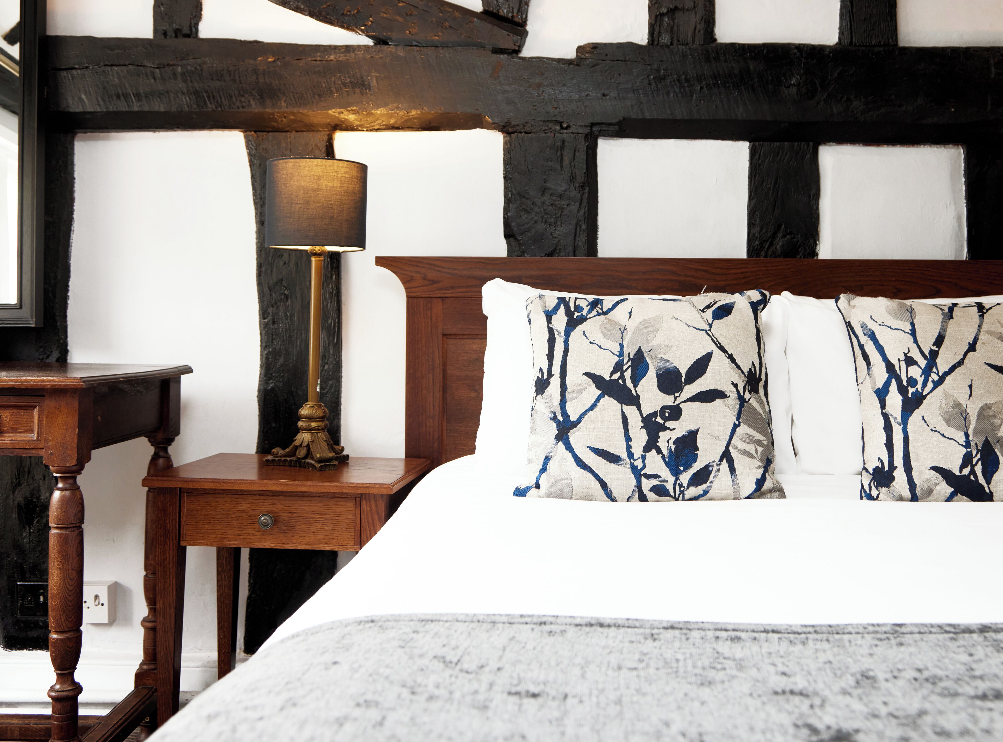 A bedroom with a wooden headboard, a bedside table with a lamp, and a bed with patterned pillows.