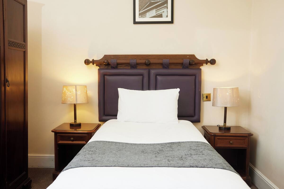 A hotel room with a bed, two bedside tables, two lamps, a headboard, and a door.