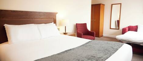 Habitación de hotel con una cama grande, cabecera de madera, un sillón rojo, un escritorio con lámpara y un armario.