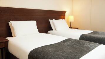 Una habitación de hotel con dos camas, cabecero de madera, ropa de cama blanca y una lámpara de noche.
