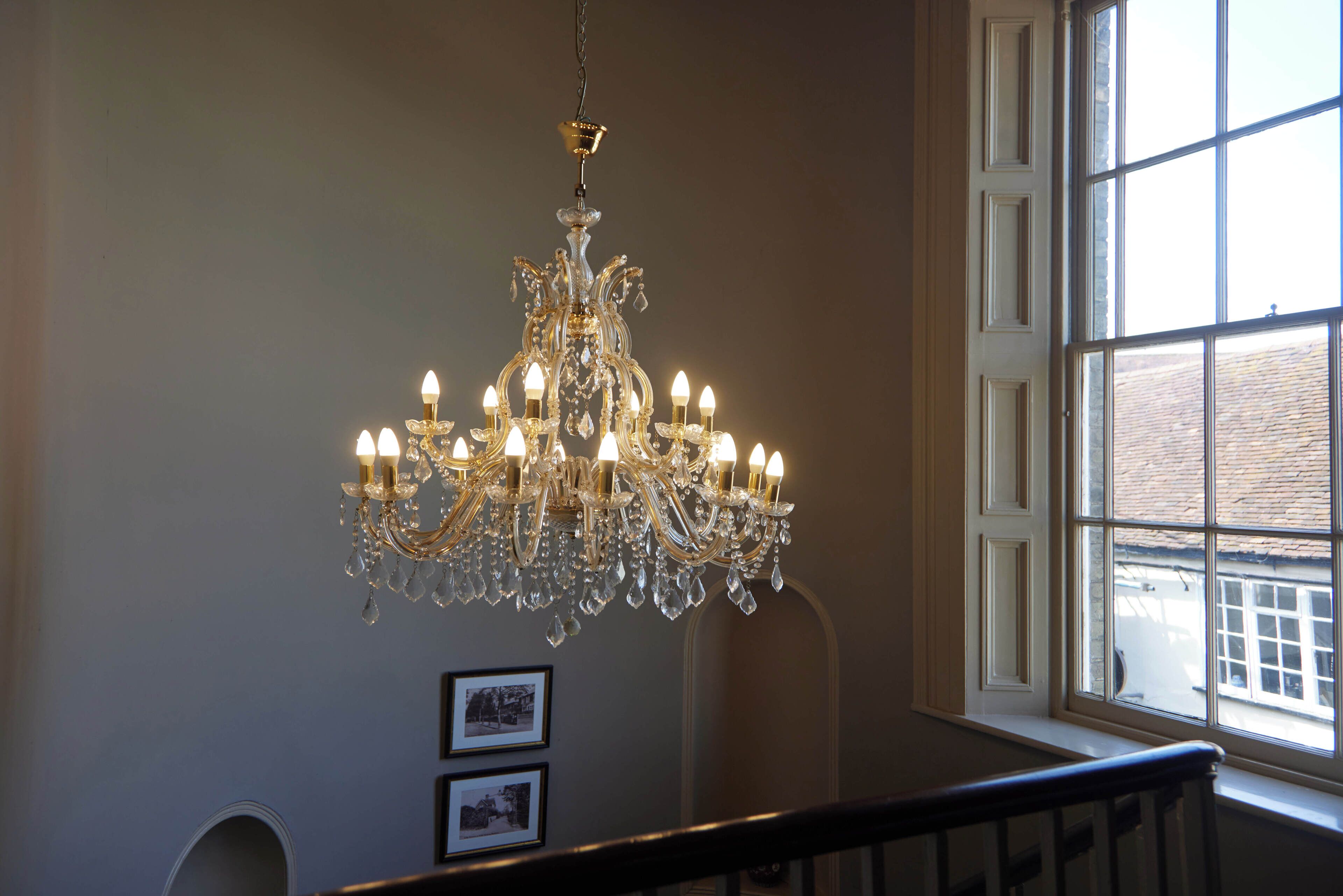 A grand chandelier with multiple lights, a staircase, and a window with a view of the outside.