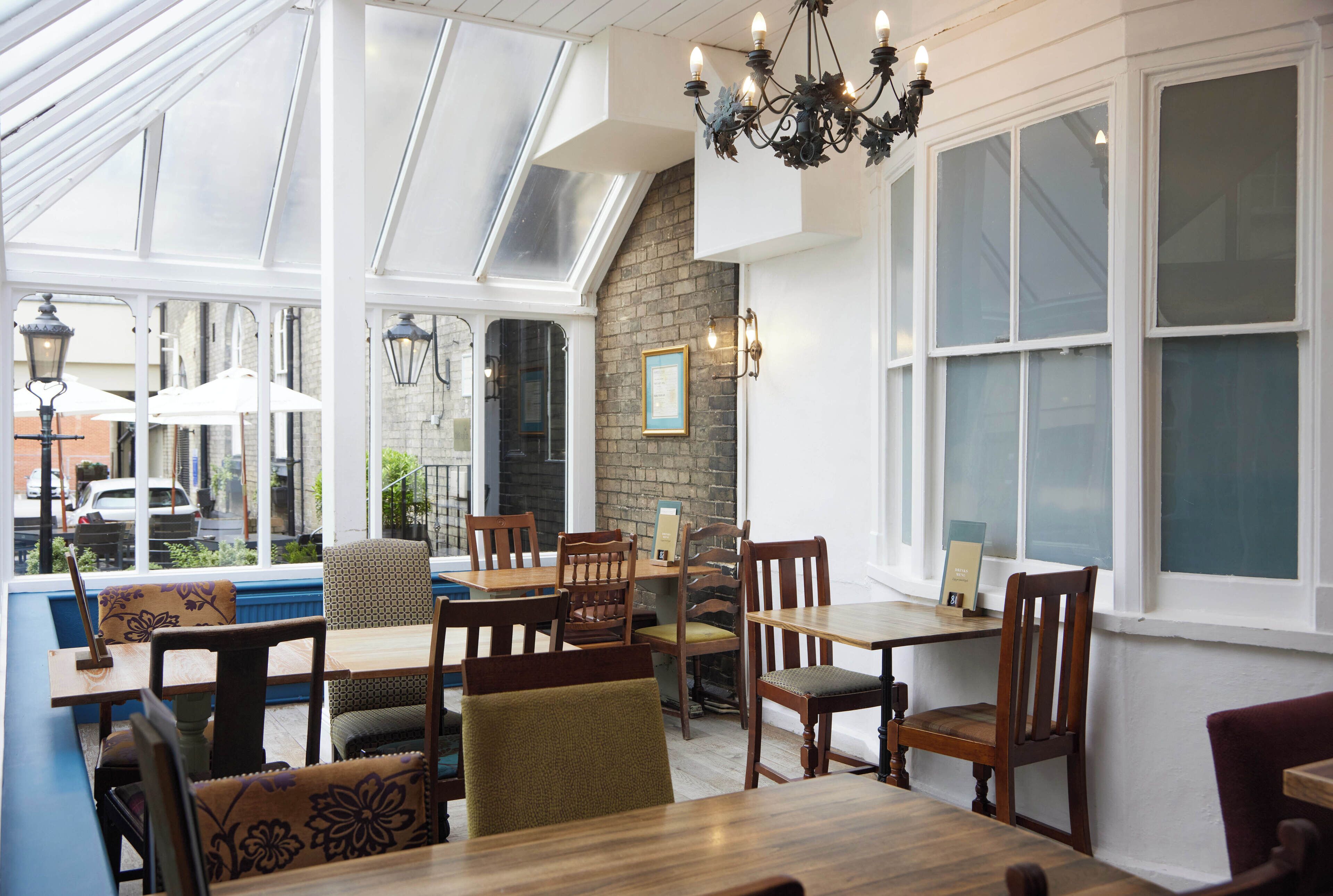 A restaurant with a high ceiling, large windows, and a brick wall.