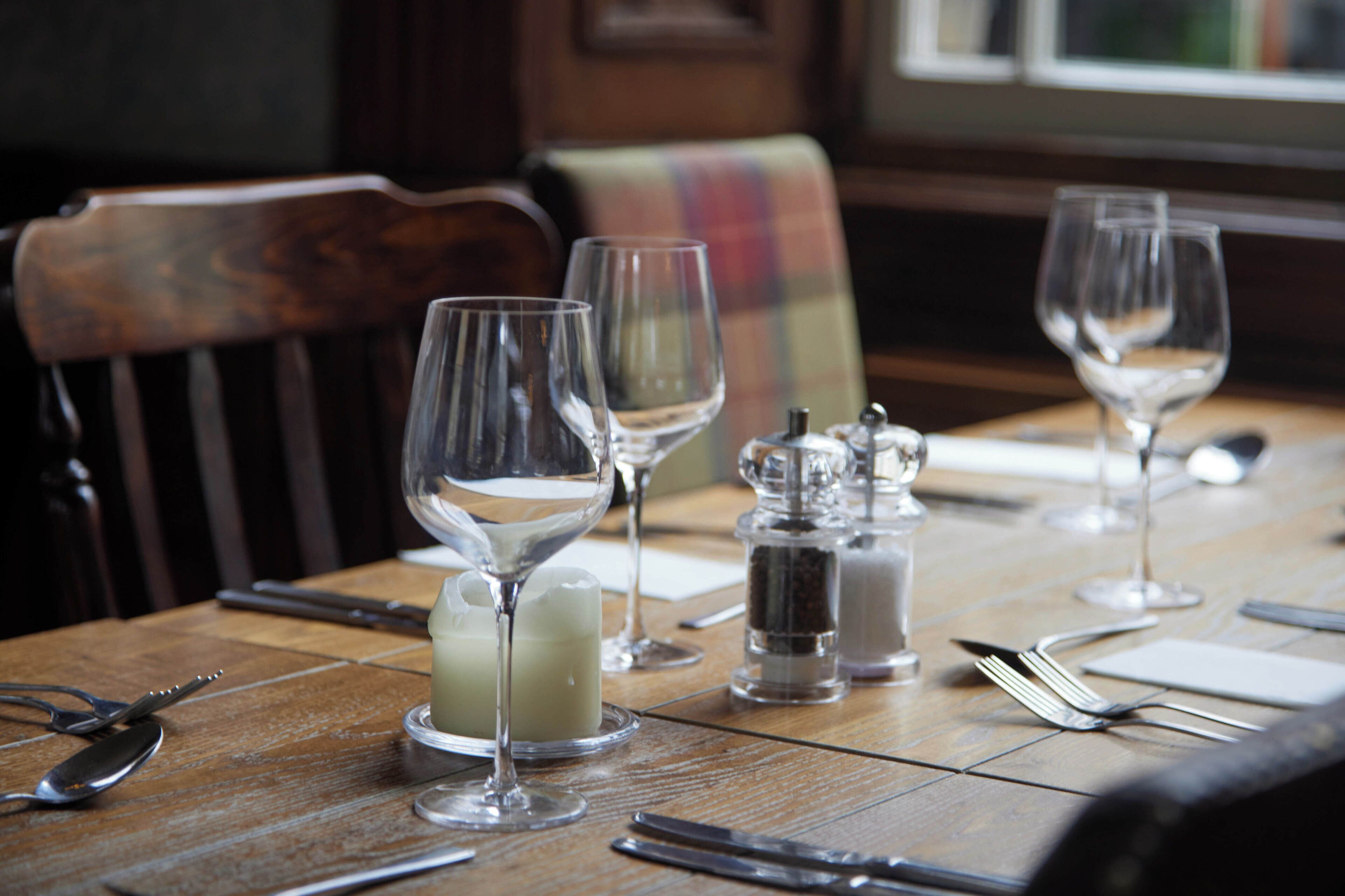 A dining table set with wine glasses, a candle, salt and pepper shakers, and cutlery.
