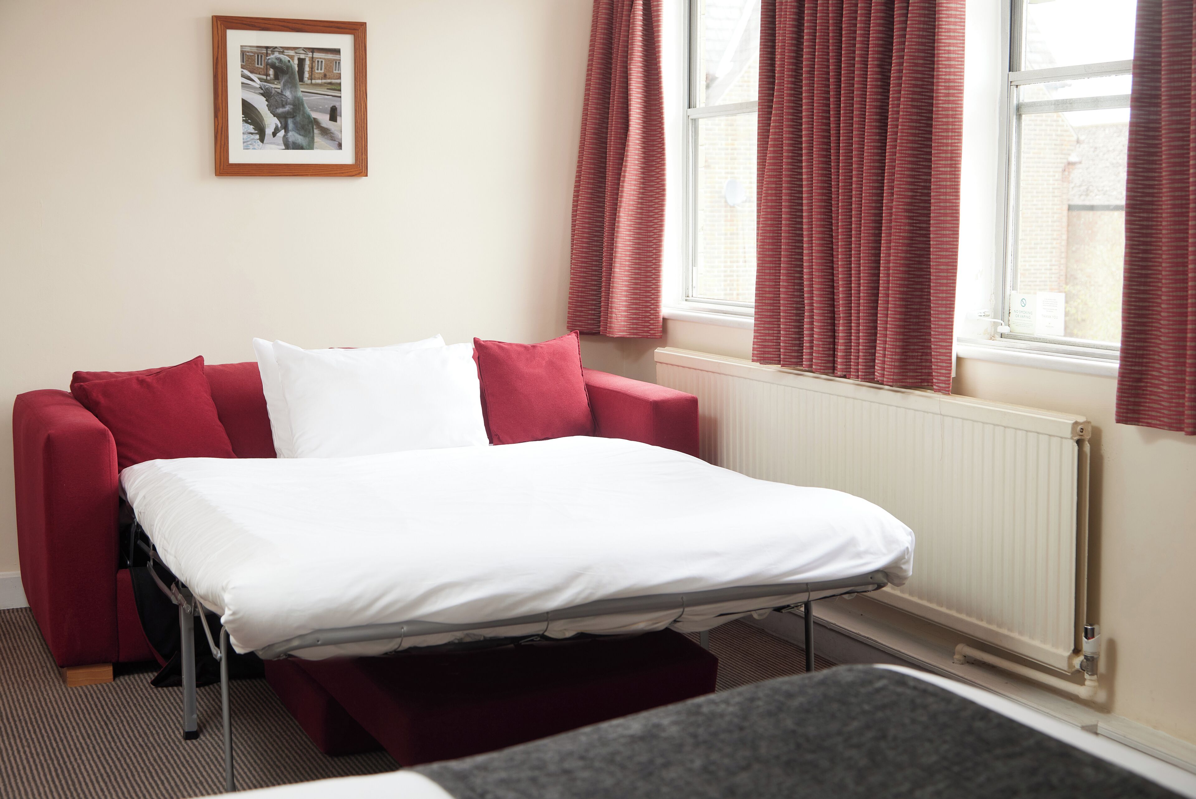 A room with a bed, a red sofa, and a window with curtains.