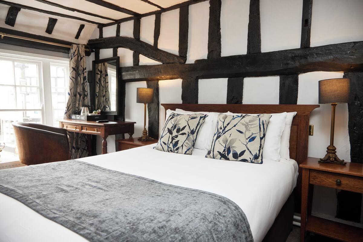 A bedroom with a large bed, a wooden nightstand, a desk, and a chair.