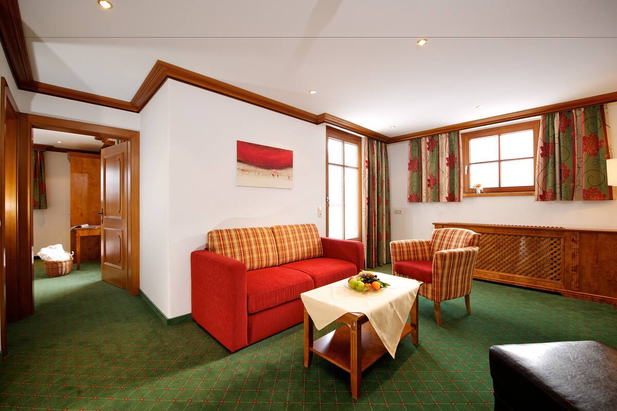 Een gezellige woonkamer met een rode bank, een houten tafel met fruit, en een vloer met een patroon.