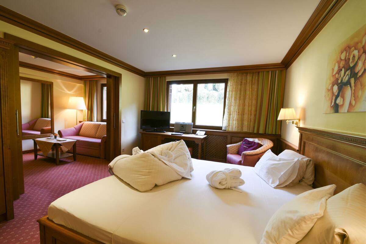 Hotelkamer met een groot bed, televisie, bureau en zithoek met een bank en fauteuil.