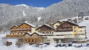 Un hôtel à plusieurs étages doté de balcons, avec une piste de ski en arrière-plan et un parking rempli de voitures.