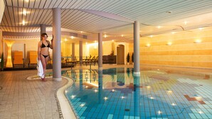 Un espace piscine doté d’un sol carrelé, d’un plafond incurvé et d’un coin salon avec des chaises et des tables.