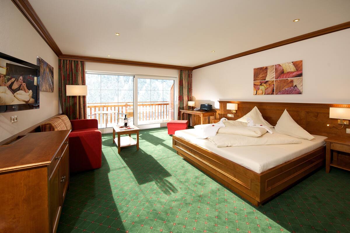 Een hotelkamer met een groot bed, een bureau, een stoel, een televisie en een balkon.