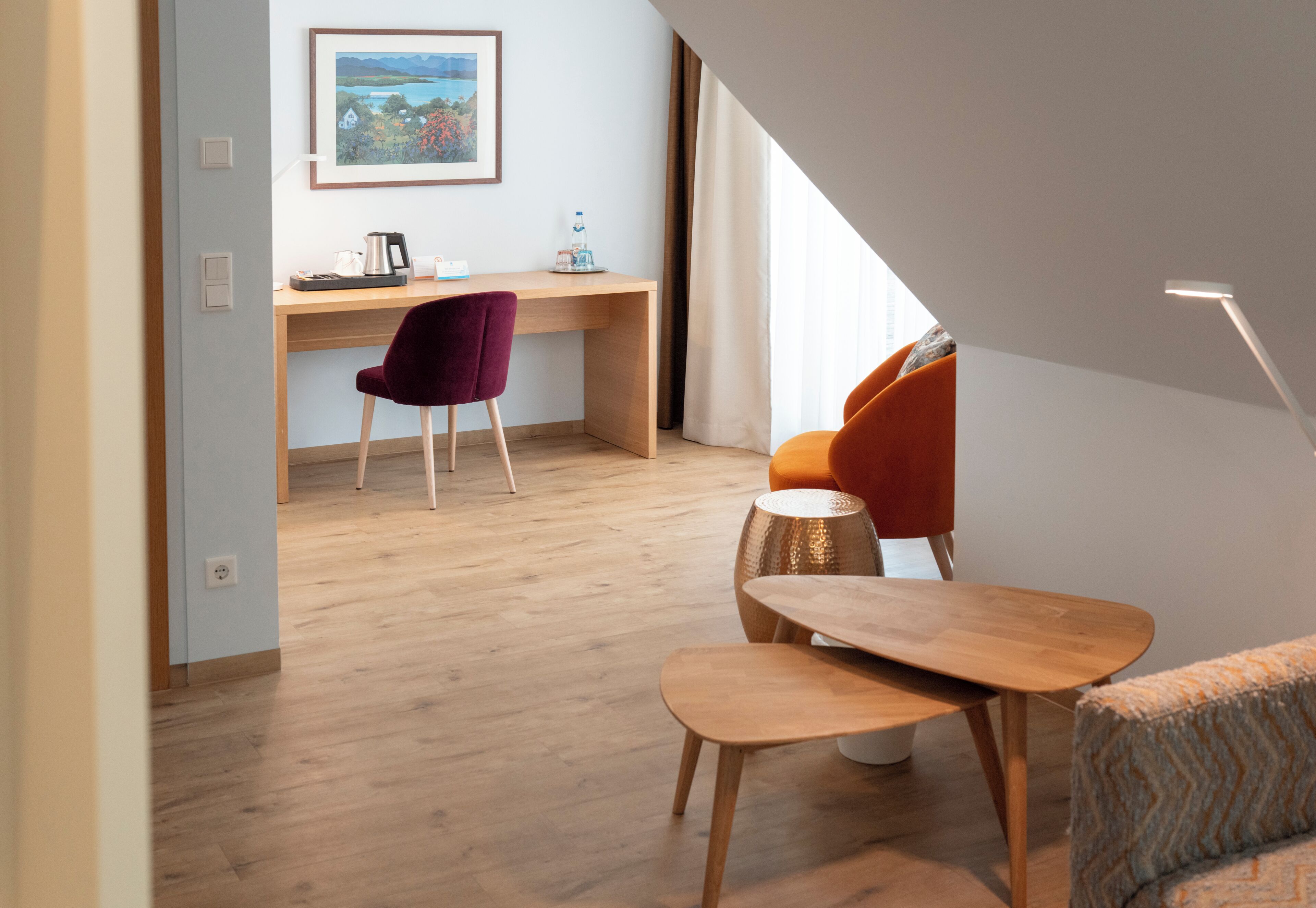 A modern room with a wooden desk, a purple chair, an orange sofa, and a small wooden table.