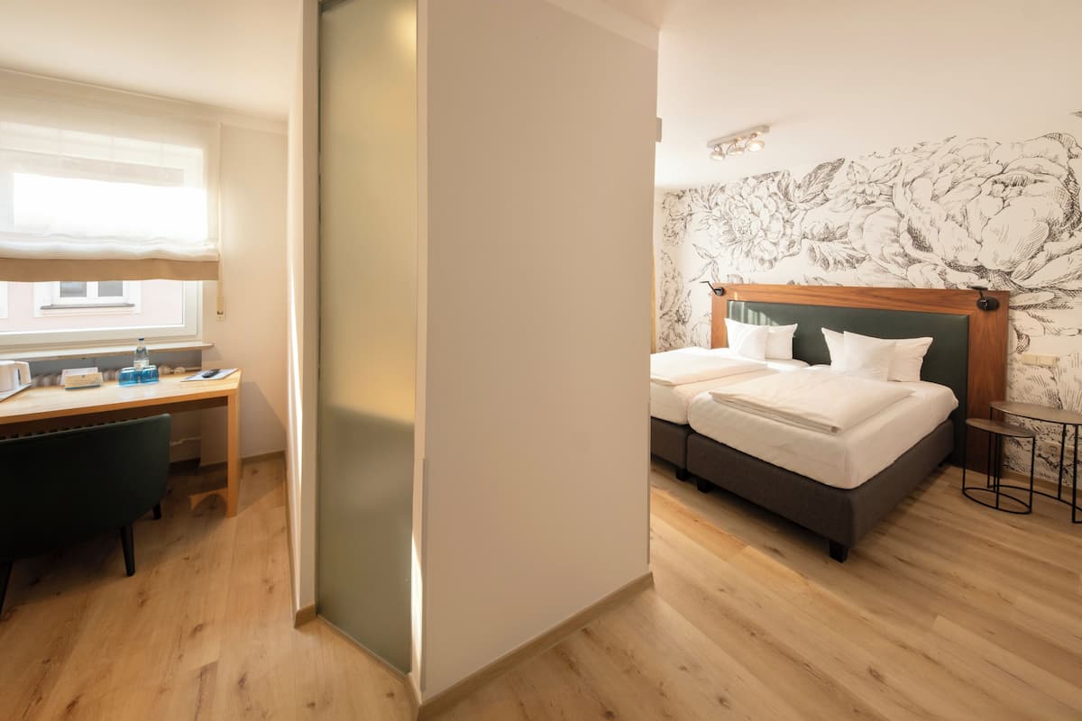 A hotel room with a bed, a desk, a chair, a small table, and a window.