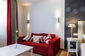 Ein rotes Sofa mit floralen Kissen, ein weißer Tisch mit einer Vase und eine Lampe auf einem kleinen weißen Beistelltisch.