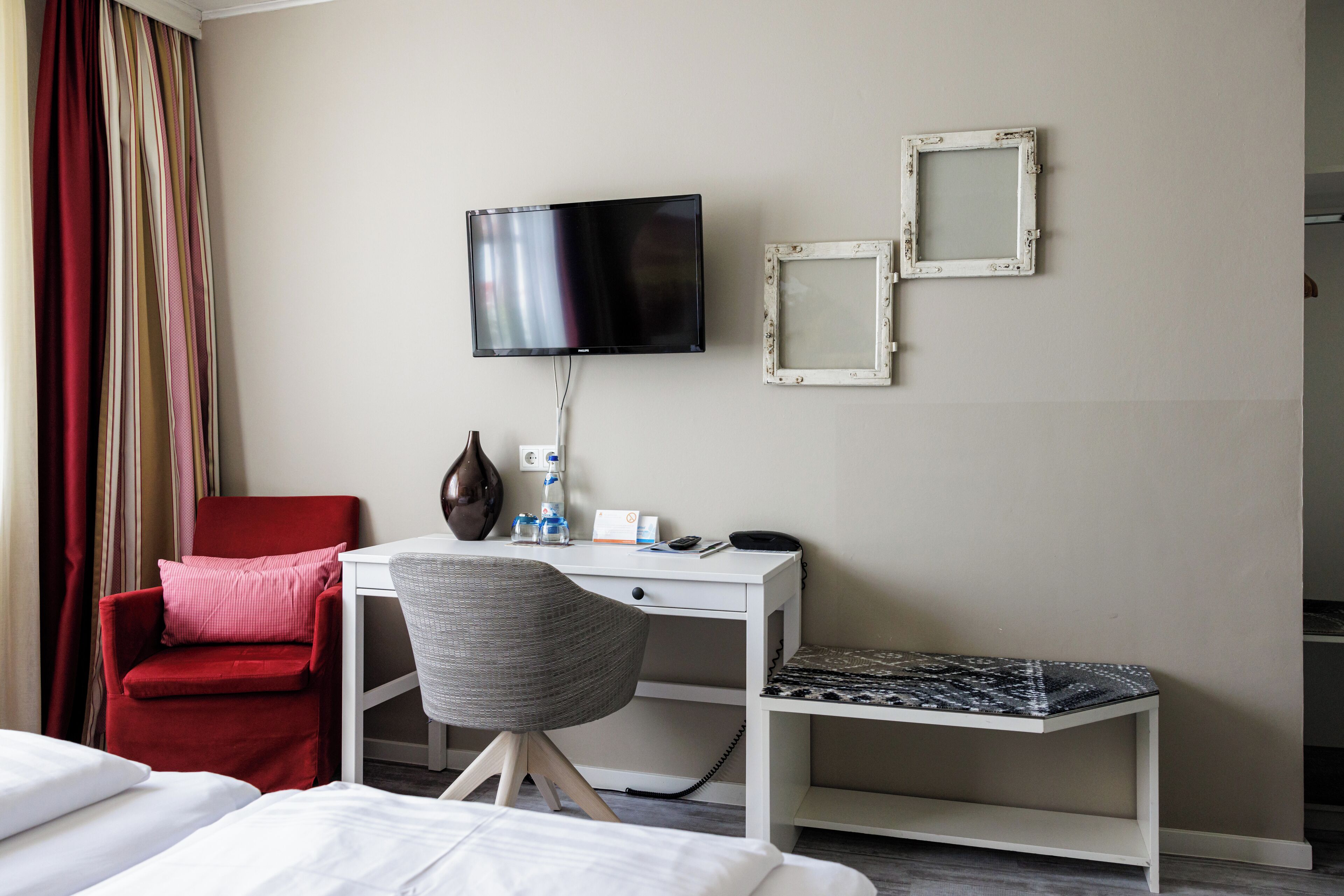 Habitación de hotel con cama, escritorio con silla, televisor y dos cuadros en la pared.