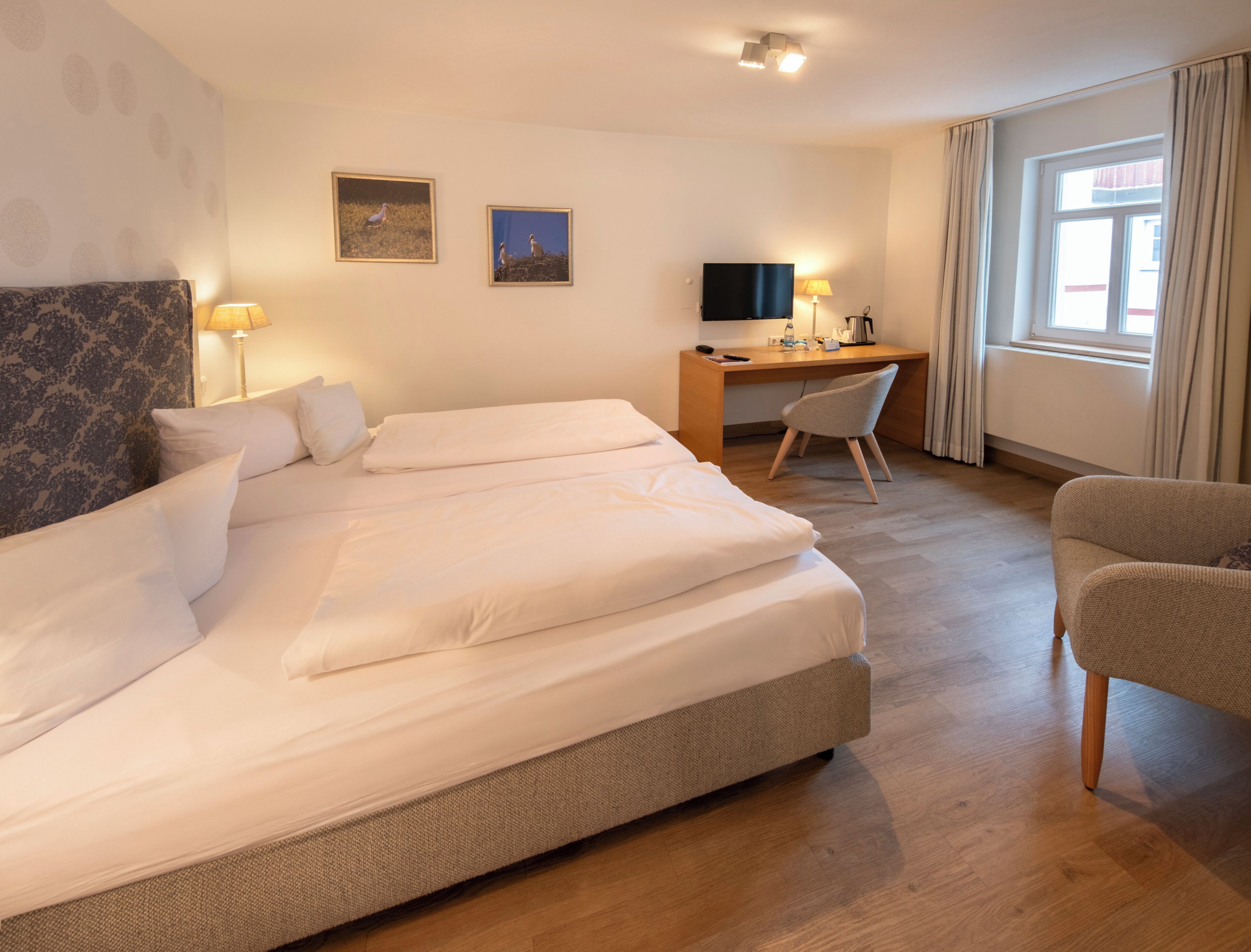 Habitación de hotel con una cama grande, un escritorio, una silla, un televisor y dos cuadros en la pared.