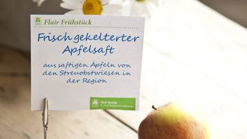 A wooden table with apples, a glass of amber liquid, and a sign about fresh apricots.