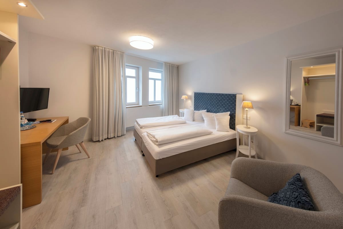 A hotel room with a bed, a desk, a chair, a TV, and a mirror.