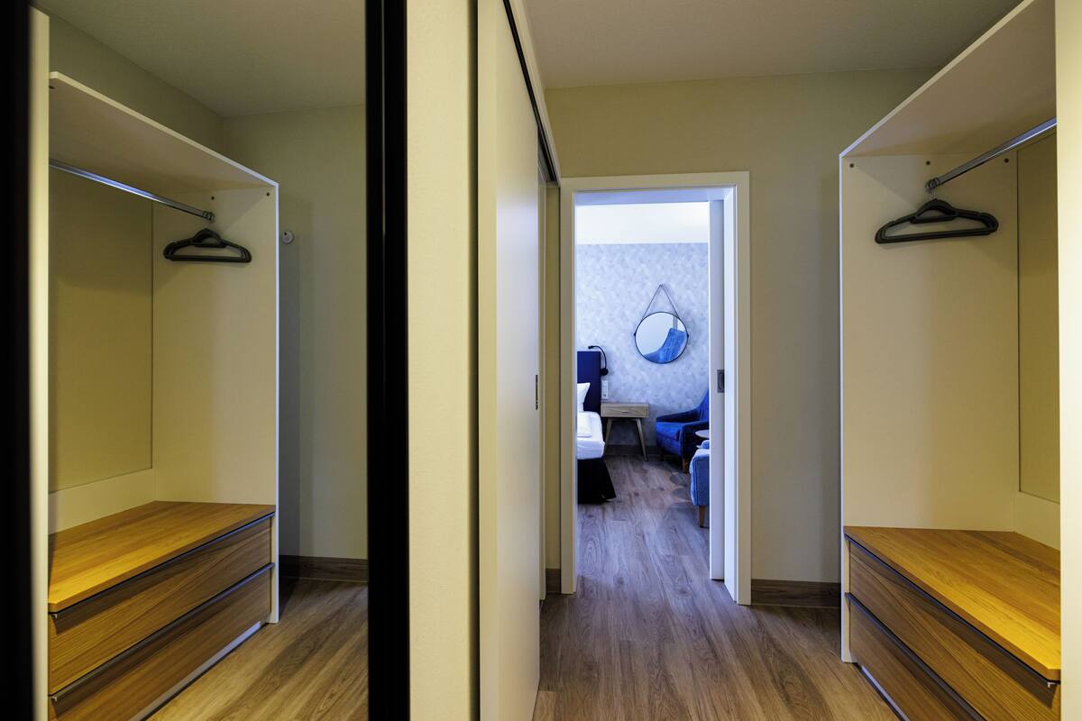 A hallway with wooden flooring and a mirror on the wall. There are two wooden cabinets on either side of the hallway.