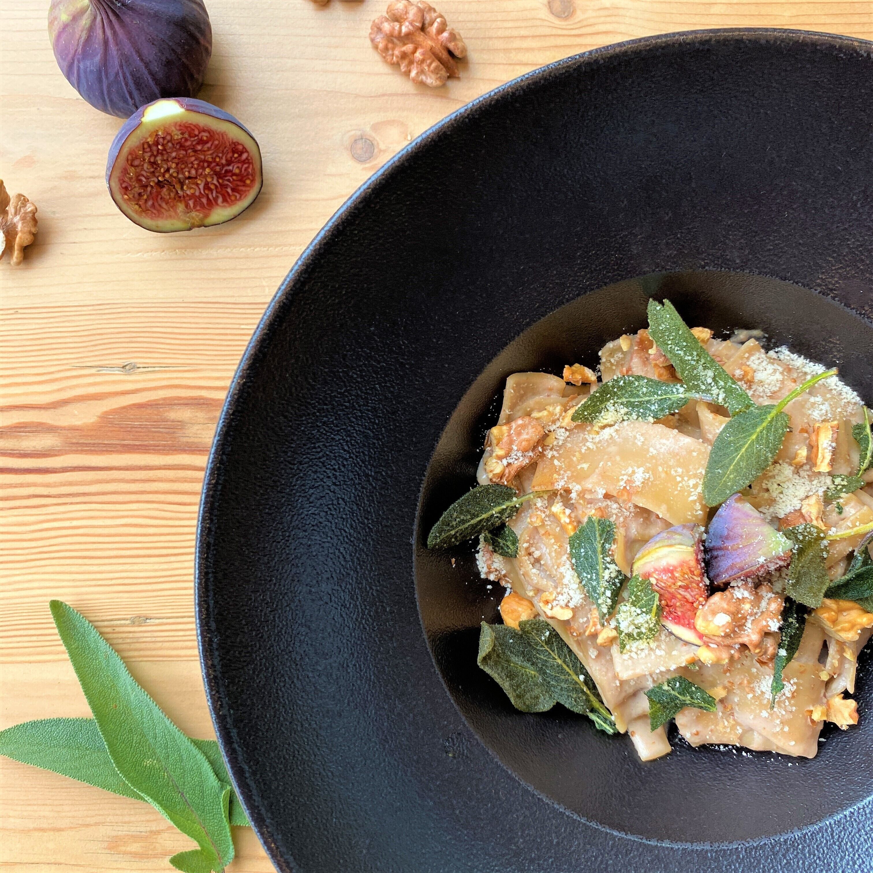 A dish with pasta, walnuts, and herbs on a black plate.