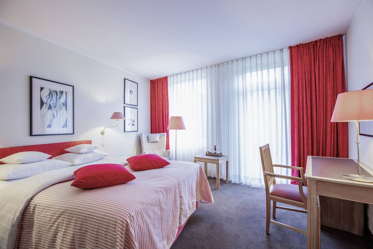 A hotel room with a bed, a desk, a chair, and a small table.