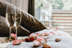 Two champagne flutes on a textured surface with rose petals and strawberries. - Romantik Hotel Landschloss Fasanerie (Zweibruecken)
